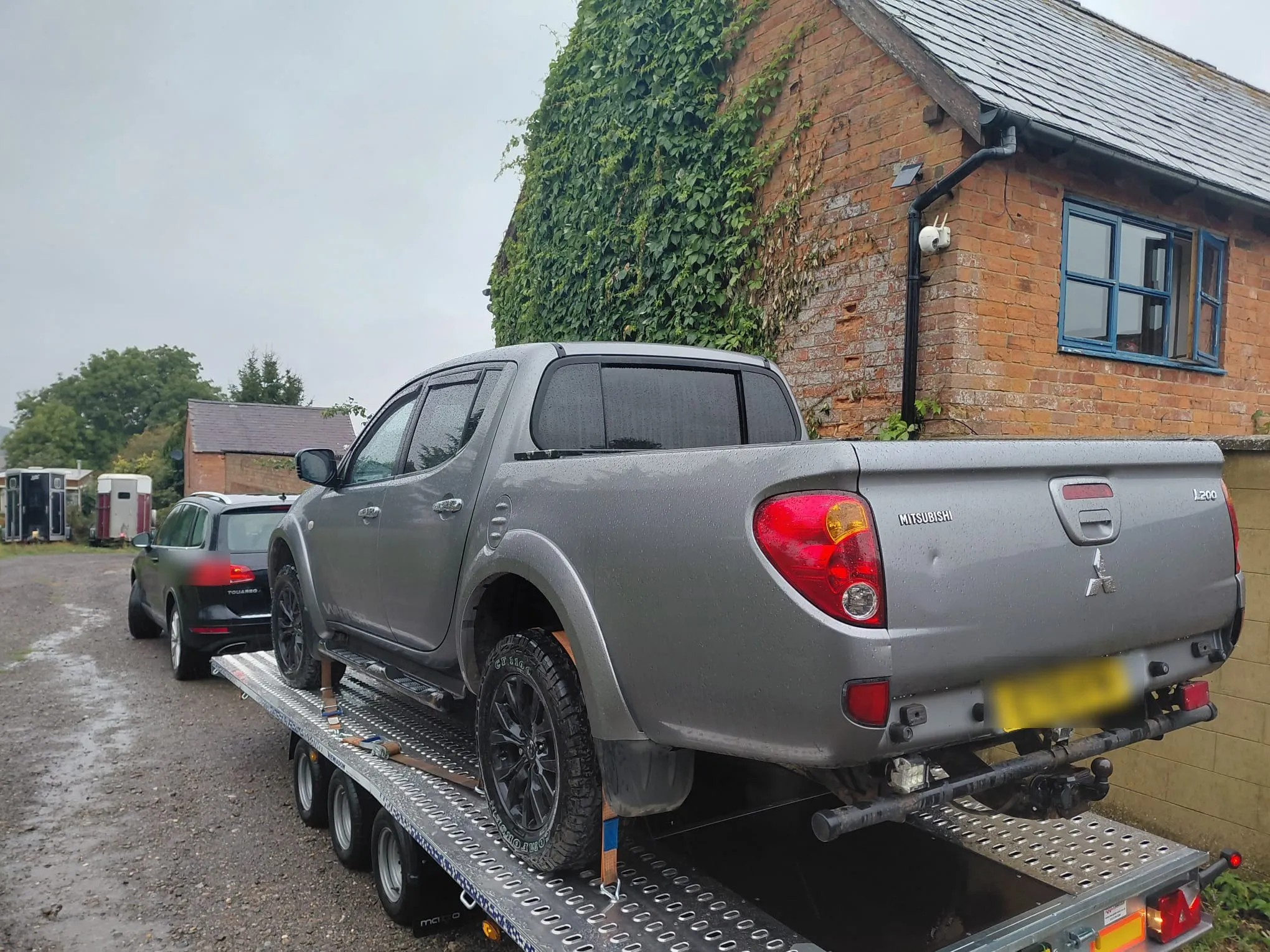Grey Mitsubishi L200 pickup on the trailer by a brick barn