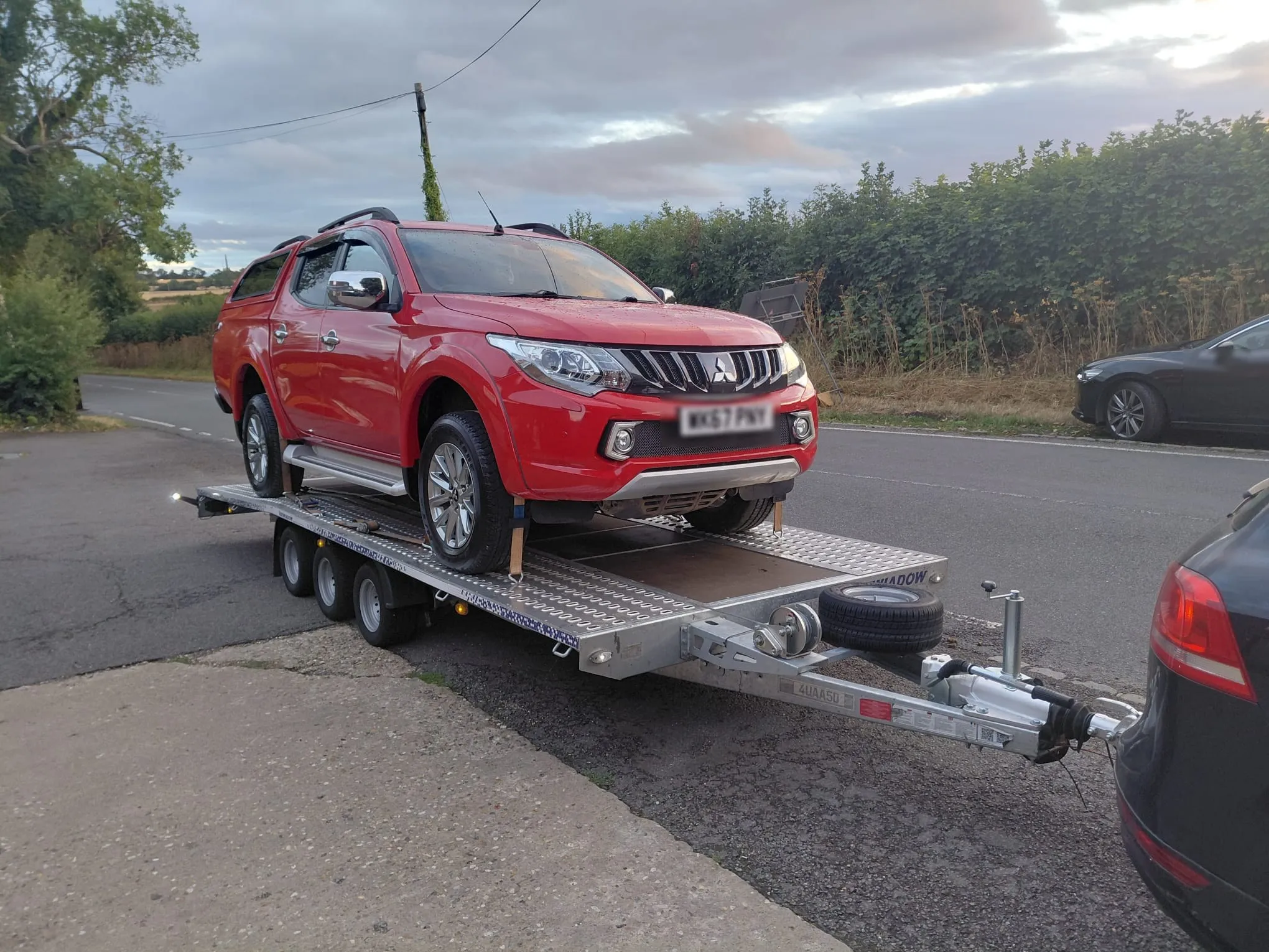 Red Mitsubishi L200 pickup on the trailer at the roadside