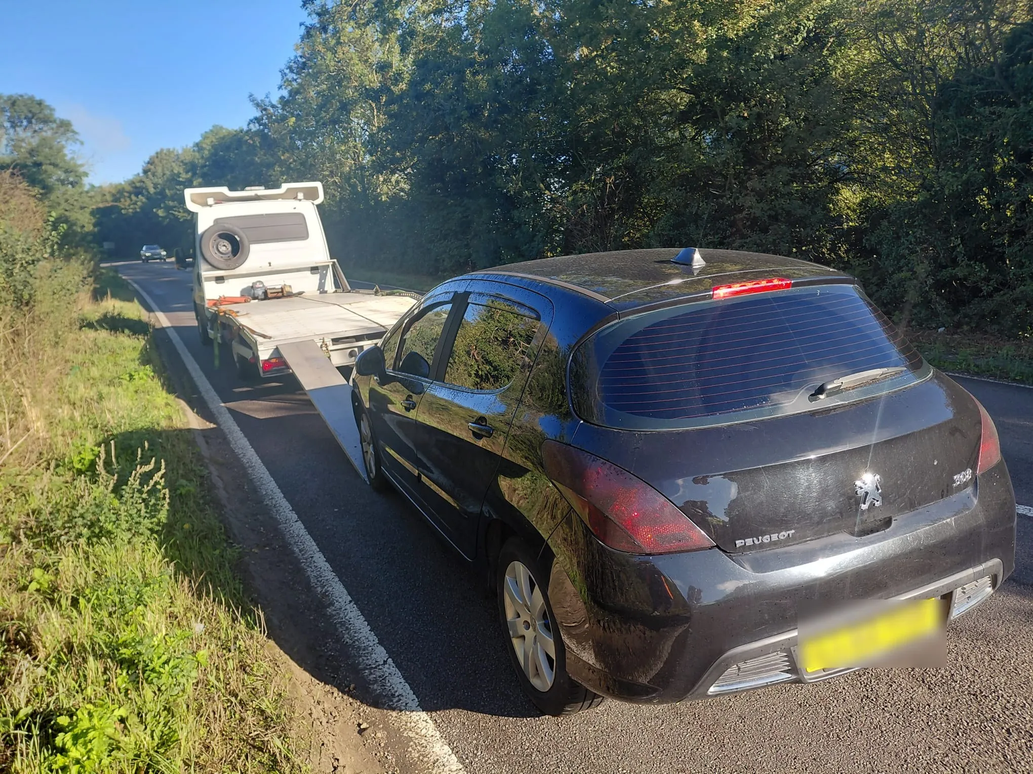 Black Peugeot 308 loaded for transport at the roadside